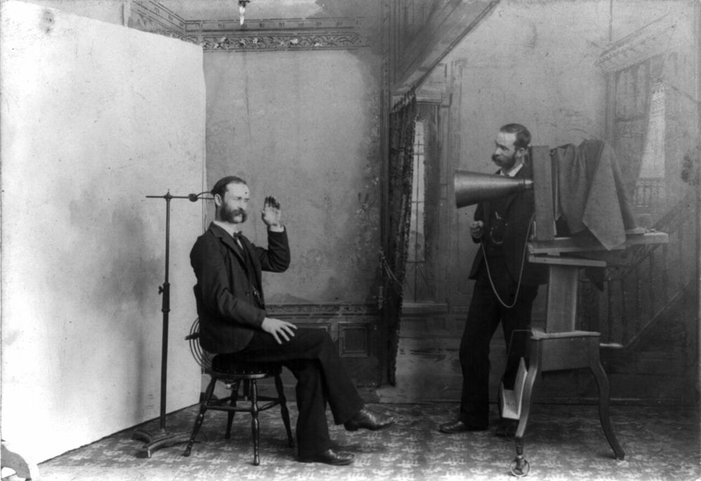 TITLE: A photographer appears to be photographing himself in a photographic studio: Wheeler, Berlin, Wis. A composite photograph showing a photographic studio interior. One man is seated on a stool near an adjustable clamp to hold his head steady during a long portrait exposure. The second man, stan
