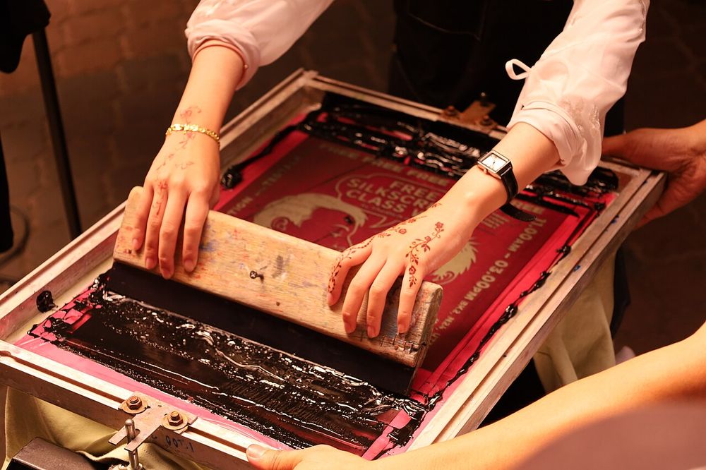 A serigrapher demonstrating screen painting by pulling the squeegee to create a design at the TEDxUTM Conference in Johor Bahru, Malaysia on 25 May 2025.